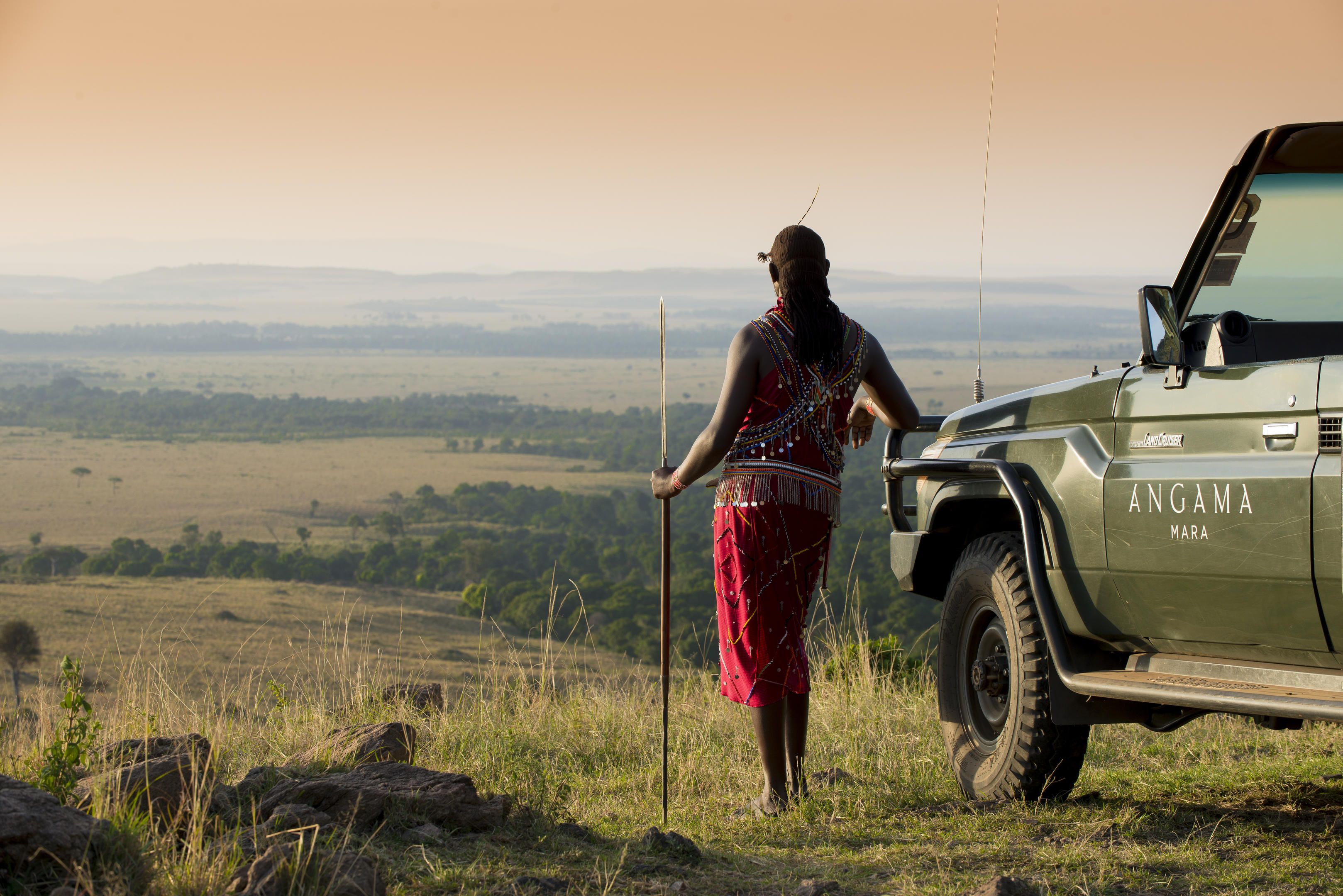 Masai warrior next to game drive vehicle on a hill by Angama Mara Kenya Masai Mara