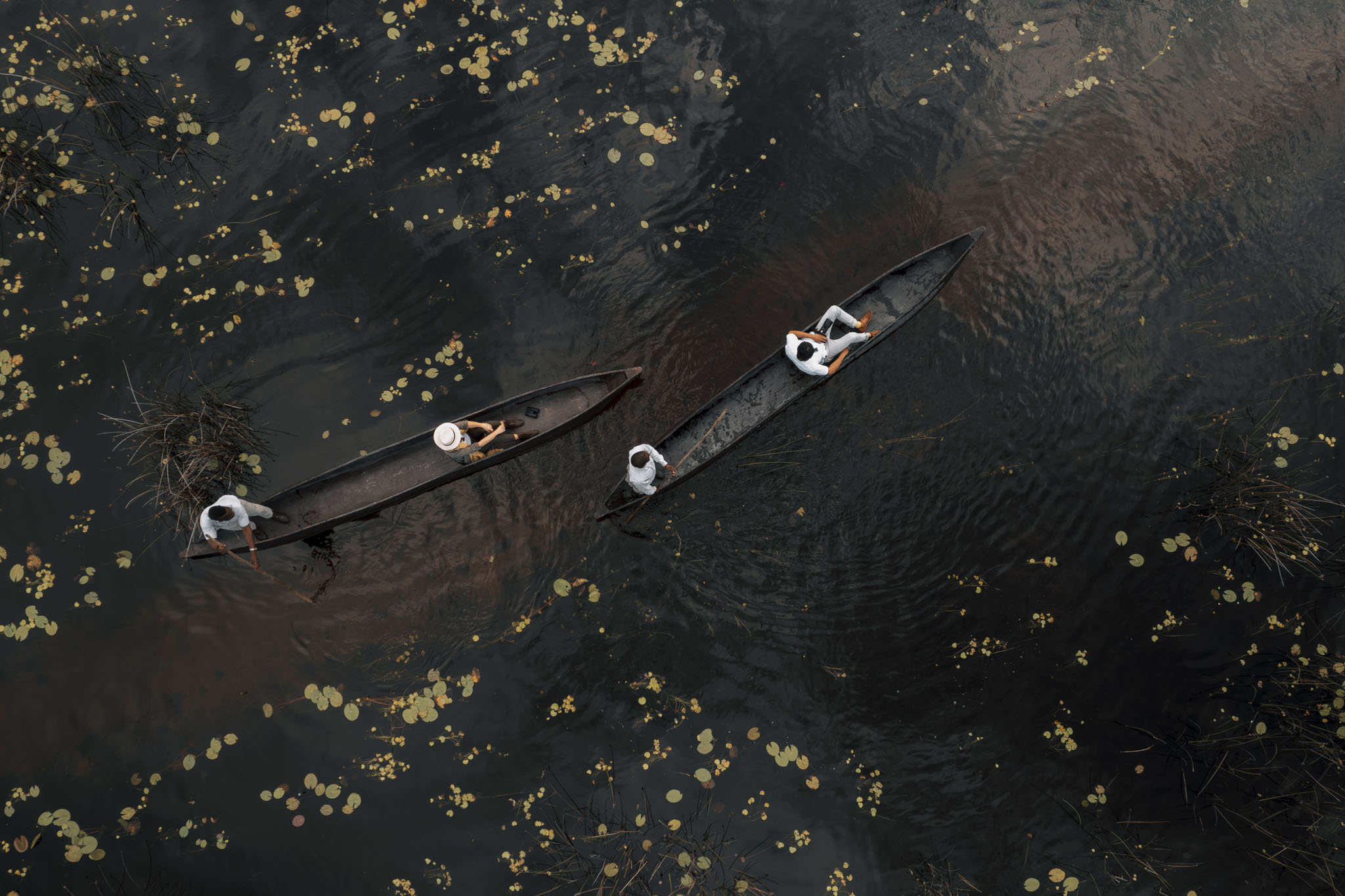 two black mokoros in black water with guests filmed from above at Vumbura Plains Camp Wilderness Okavango Delta