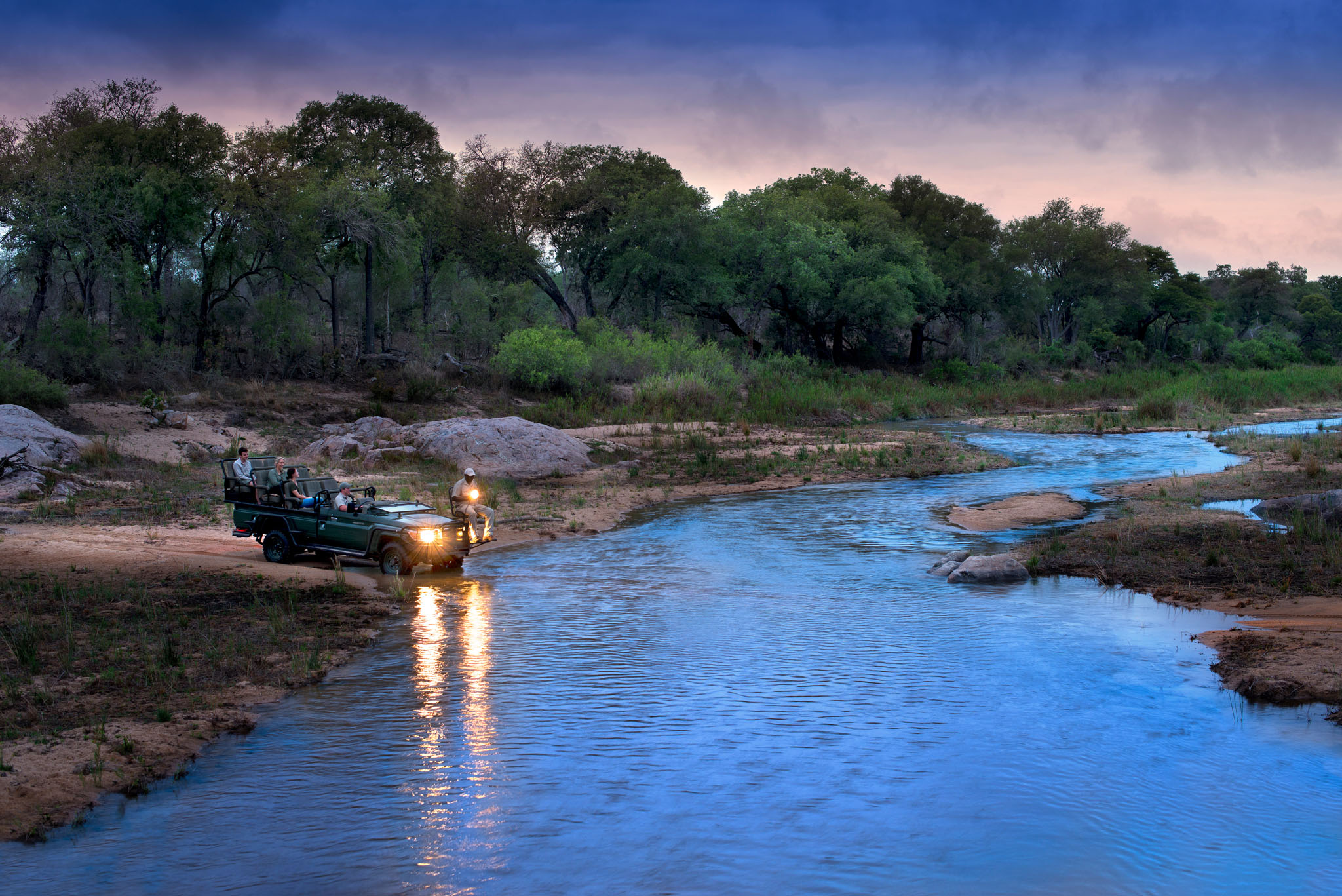 safari vehicle crossing river at sunset at andBeyond tengile river lodge