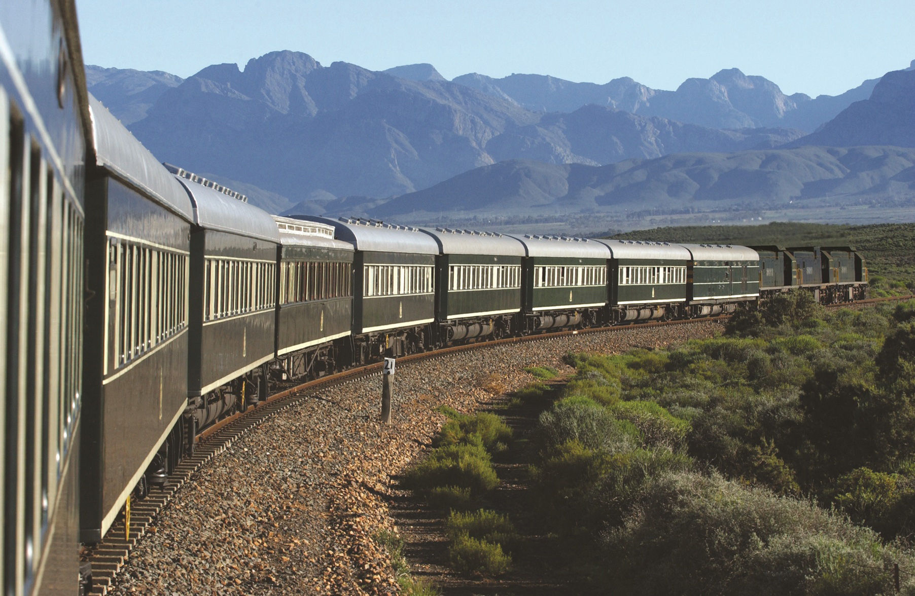 train snaking through countryside in south Africa with big mountains backdrop at Rovos rail luxury train safaris