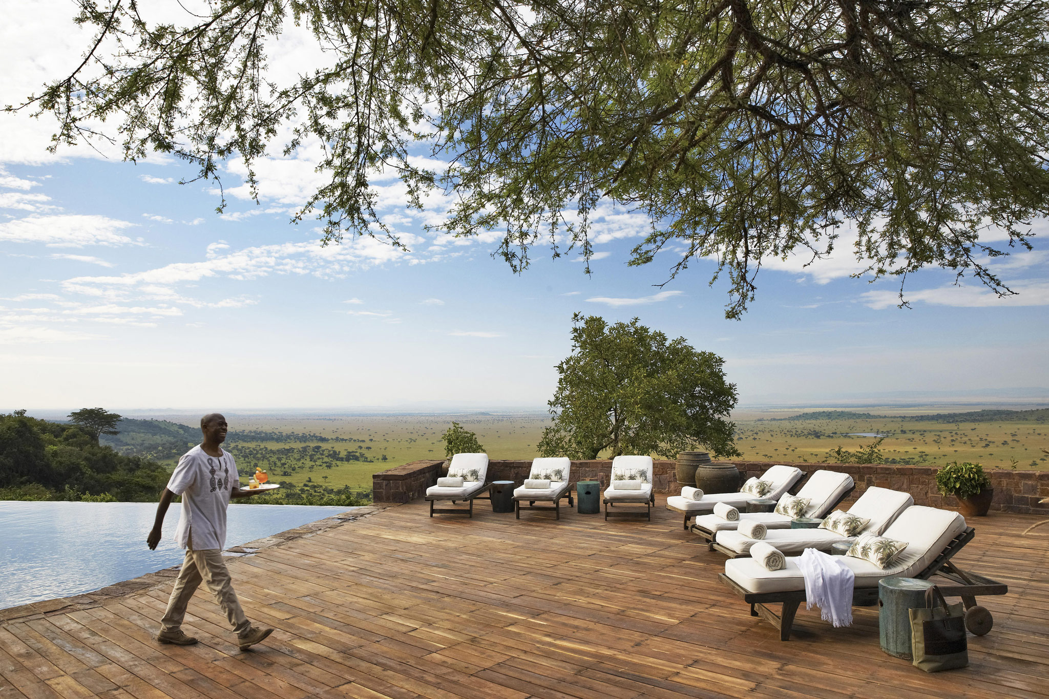 staff serving guests at the main pool of lady guest in the main rim pool of Singita Sasakwa lodge overlooking the Serengeti