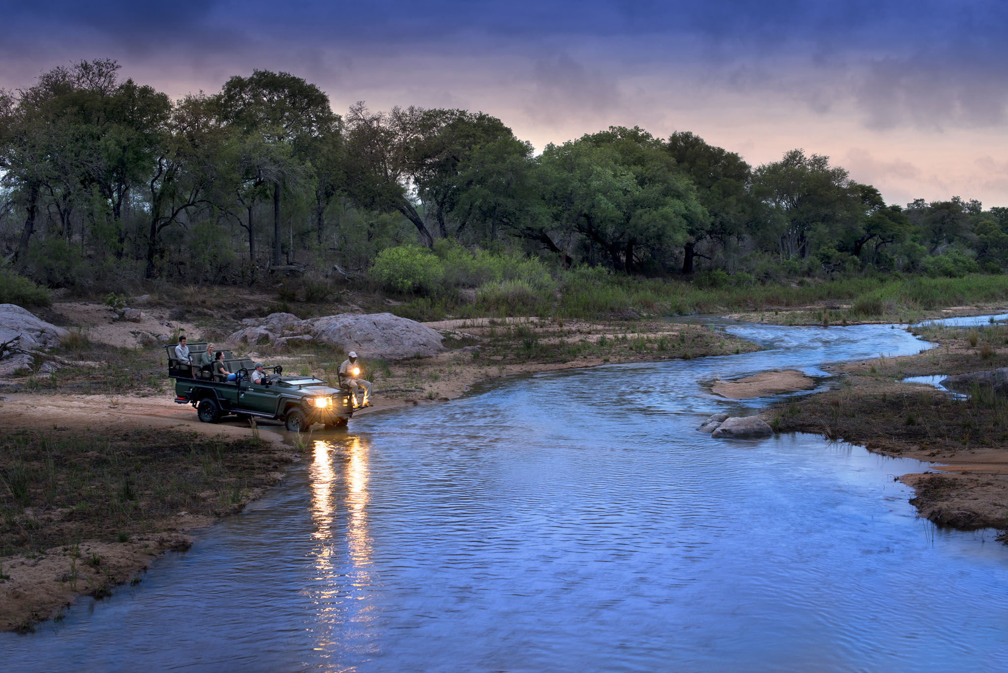 safari vehicle crossing river at sunset at andBeyond Tengile river lodge