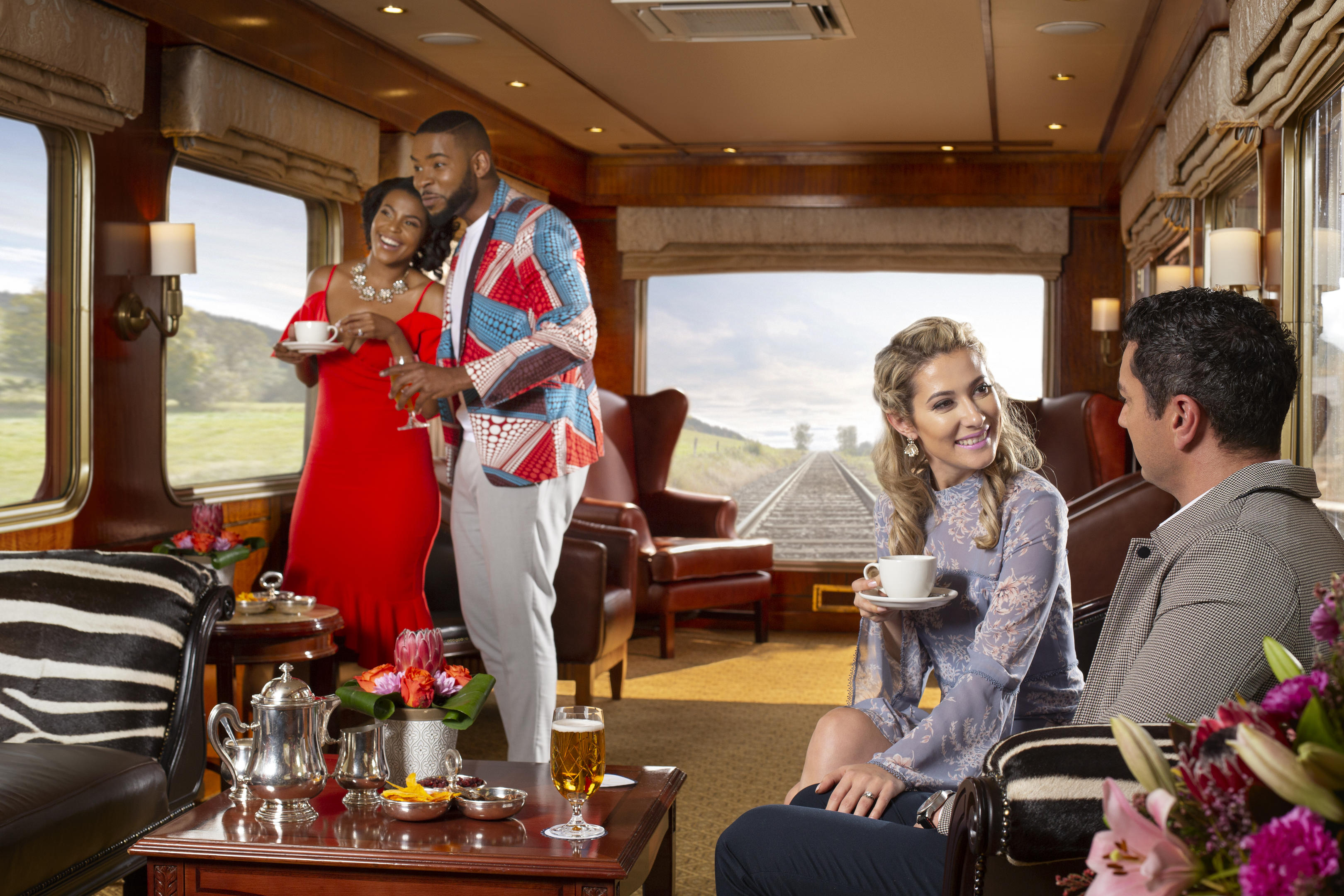 three guests having tea in the observation cart of Blue Train South Africa with views of tracks behind train