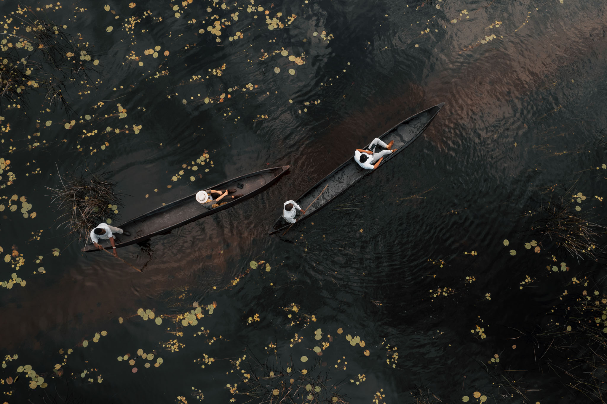 two black mokoros in black water with guests filmed from above at Vumbura Plains Camp Wilderness Okavango Delta